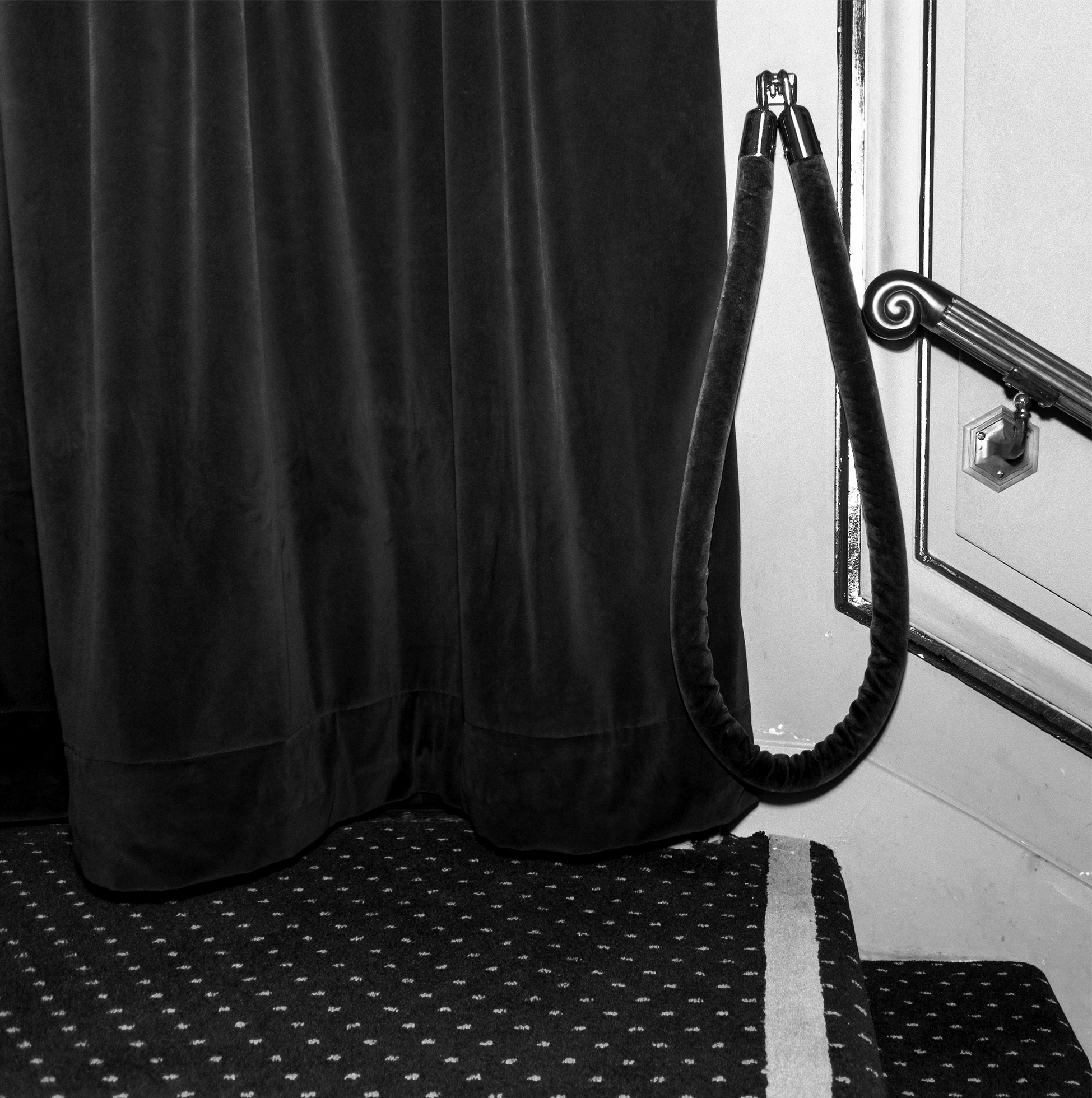 Carpeted steps in a theater lead to a heavy velvet curtain and velvet rope hanging against a wall.