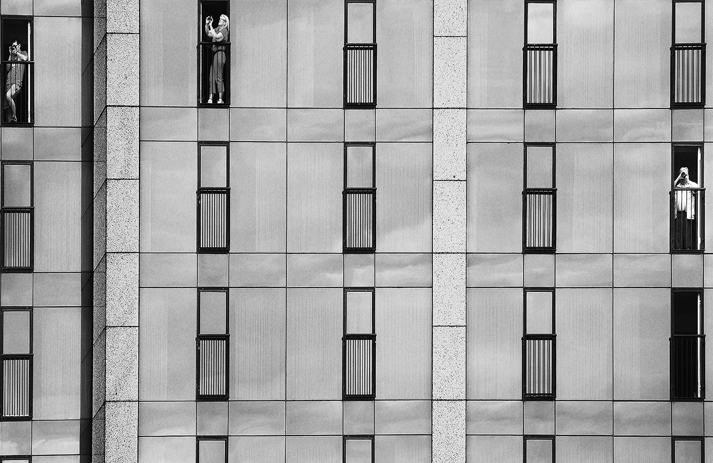 Three tourists stand on their tiny hotel balconies photographing Niagara Falls from the Canadian side.