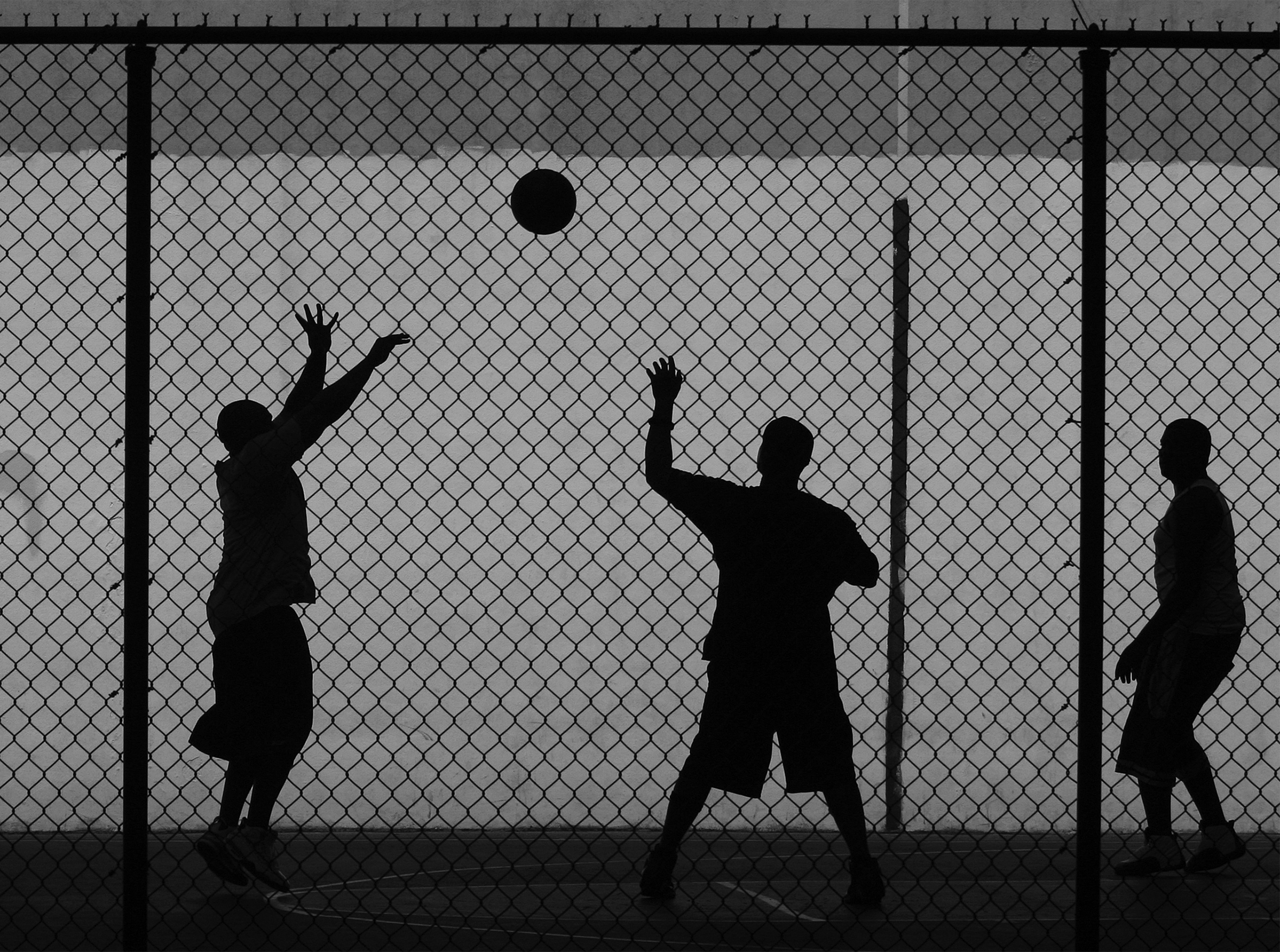 Three street ballers at a playground in Manhattan seen through a chain-link fence.