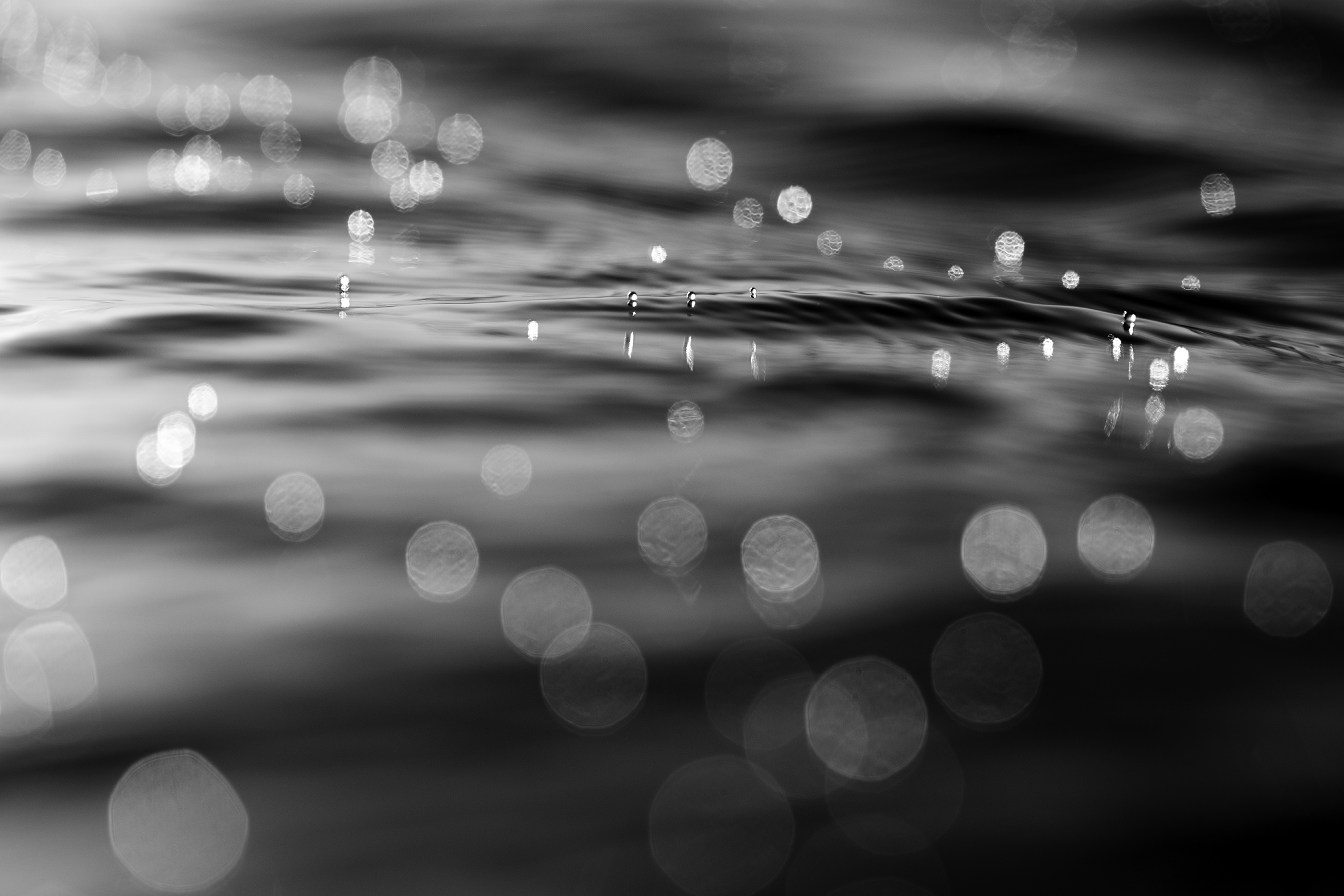 Ripples in the water after a wave has crashed with what look like many orbs of light floating down from the crashing wave’s energy, but what the photographer affectionately calls “little sea pearls.”